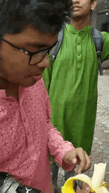 a man in a green shirt is standing next to a woman in a pink shirt eating a banana peel .