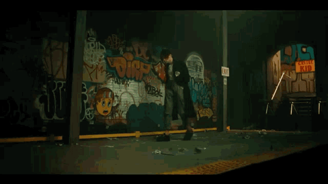 a woman is standing in front of a graffiti covered wall with a sign that says exit