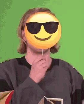 a man wearing sunglasses and a smiley face mask is holding a lollipop in front of his face .