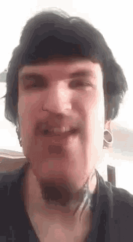 a close up of a man 's face with a tattoo on his neck and a nose ring .