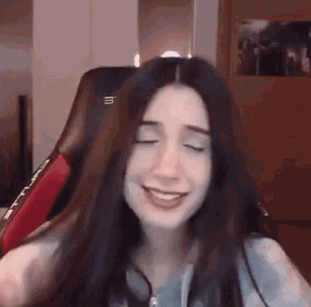 a woman with long dark hair is sitting in a gaming chair with her eyes closed and smiling .