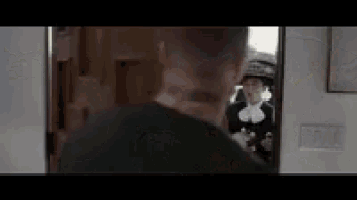 a man is standing in a doorway looking at a woman in a hat in a mirror .