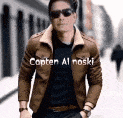 a man wearing sunglasses and a brown jacket is standing on a street .