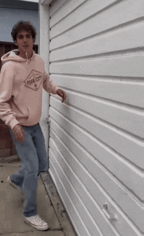 a man wearing a pink park city hoodie is standing in front of a white garage door