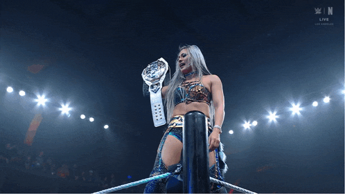 a woman in a wrestling ring holding a championship belt with a w logo in the background