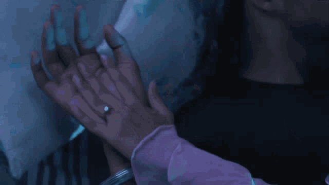 a woman in a purple shirt is laying on a bed with a man holding her hand
