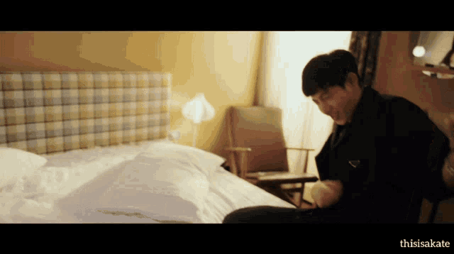 a man in a plaid headboard sits on a bed with the words thisisakate below him