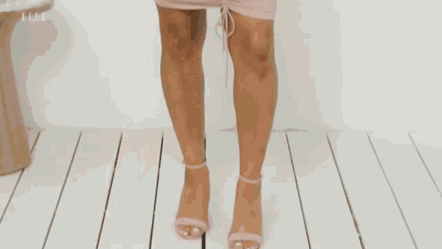 a woman in a pink dress is standing in front of a white wall and looking at the camera .