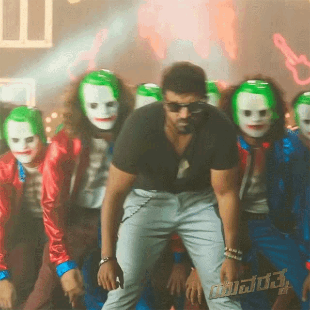 a man in a black shirt is standing in front of a group of jokers wearing green masks