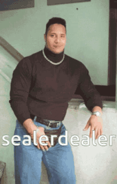 a man wearing a black turtleneck and blue jeans stands in front of a sign that says sealer dealer