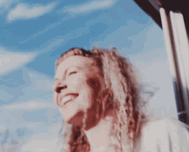 a woman with blonde curly hair is laughing with a blue sky in the background