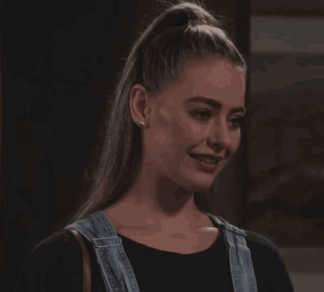 a woman in overalls and a black shirt smiles