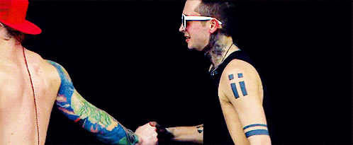 two men with tattoos on their arms are shaking hands .