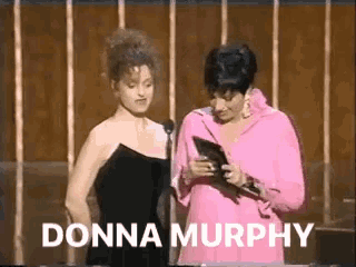 two women are standing next to each other in front of a microphone and the words donna murphy are on the screen .