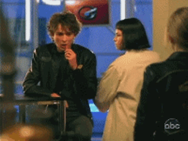 a man in a leather jacket is eating a candy bar while talking to a woman