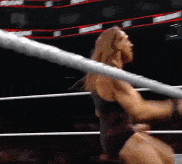 a wrestler is standing in a wrestling ring with a rope around his waist .