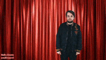 a man in a black jacket stands in front of a red curtain with the name emile atman written on the bottom