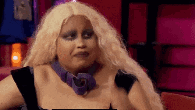 a woman with long blonde hair and a purple necklace is sitting on a couch .