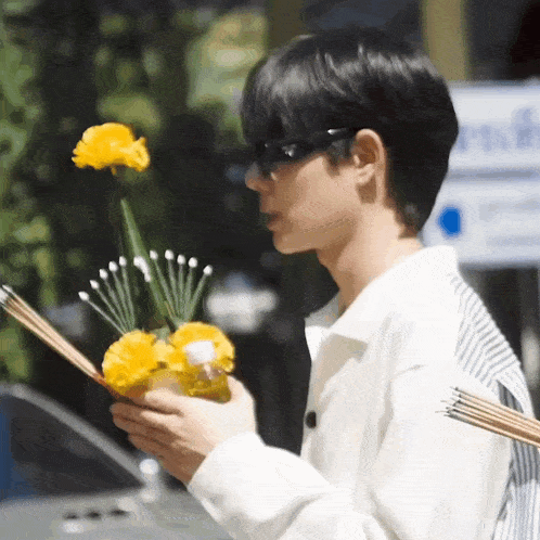 a man wearing sunglasses is holding a vase of flowers and incense sticks in his hands .