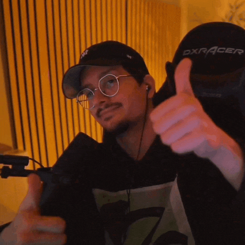 a man wearing glasses and a hat is giving a thumbs up sign