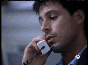 a close up of a man talking on a phone with a tv logo on the bottom right