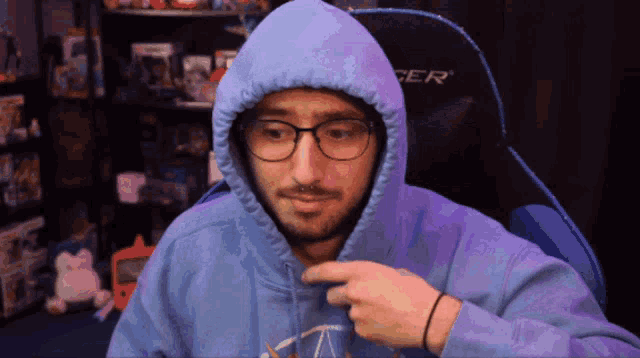 a man wearing glasses and a blue hoodie is sitting in a chair that says dxracer