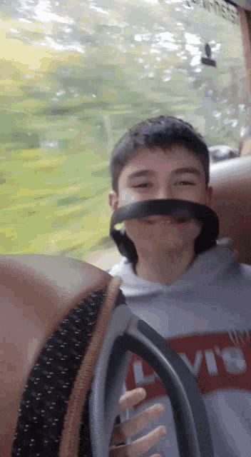 a boy wearing a levi 's sweatshirt holds a black strap around his mouth