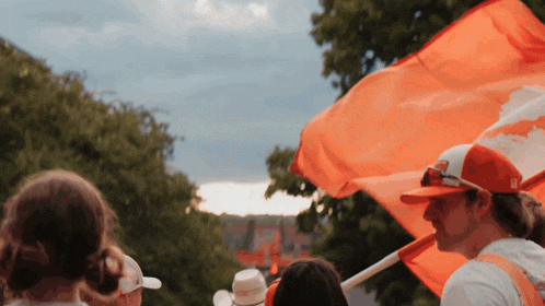 a man in a red hat holds a large orange flag