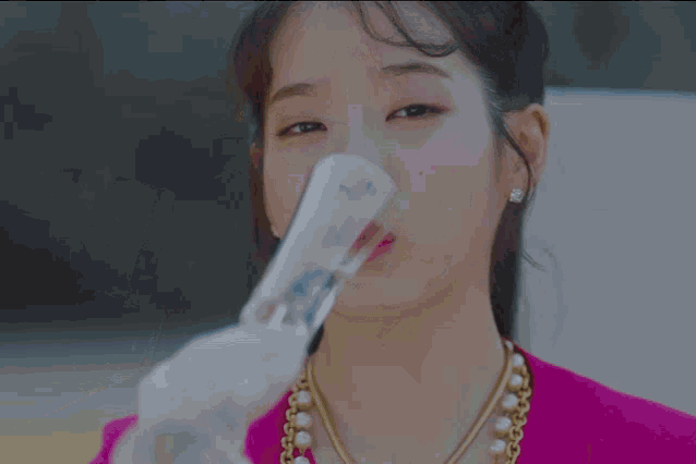 a woman in a pink shirt is drinking from a clear glass