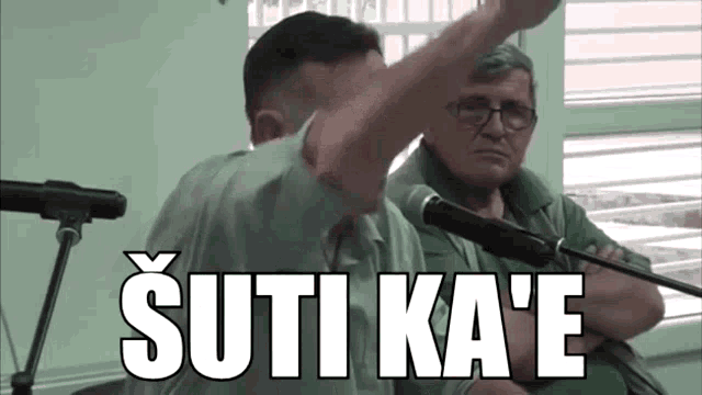 a man is giving a speech in front of a microphone and the words suti ka e are on the screen