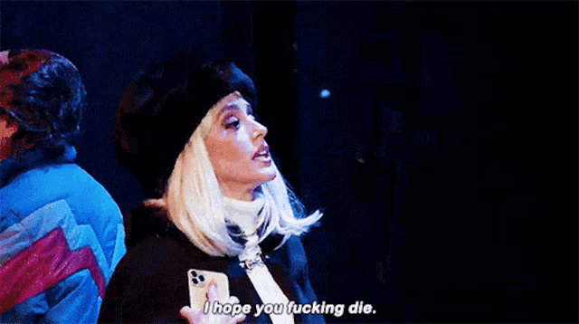a woman in a fur hat is holding a glass and a cell phone while saying `` i hope you fucking die . ''