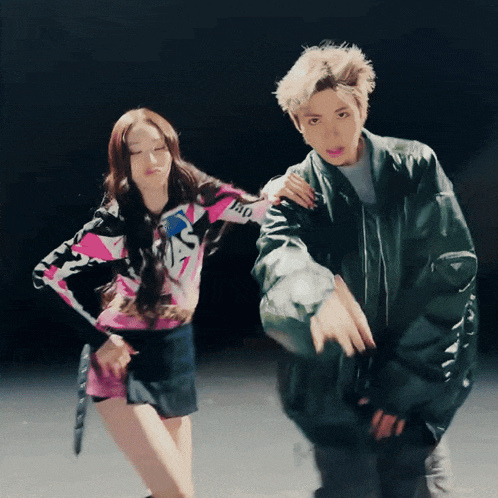 a man in a green jacket stands next to a woman in a pink shirt that says ' ao '