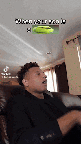 a man is sitting on a couch with a tiktok video that says " when your son is a frisbee "