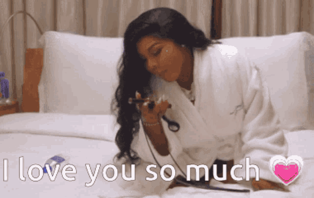 a woman in a bathrobe is laying on a bed with the words " i love you so much " above her