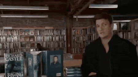 a man is standing in a library with a book titled raging castle on the shelf .