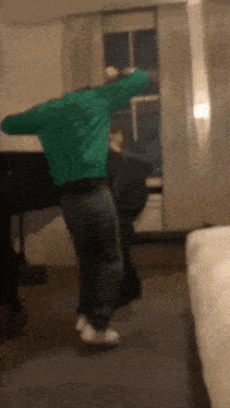 a man in a green shirt is dancing in a room