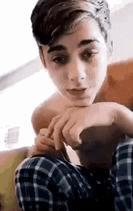 a young boy without a shirt is sitting on a couch with his hands on his face .