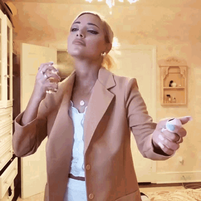 a woman in a tan jacket sprays perfume on her face