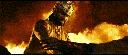 a man with a crown on his head stands in front of a fire