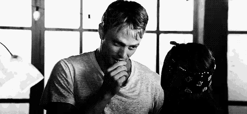 a black and white photo of a man smoking a cigarette next to a girl .