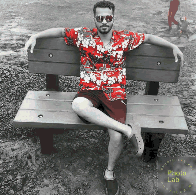 a man in a red shirt sits on a bench with his legs crossed and a photo lab logo in the background