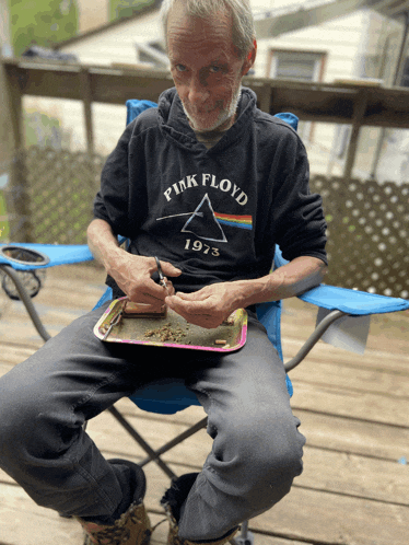 a man wearing a pink floyd 1973 sweatshirt sits in a blue chair