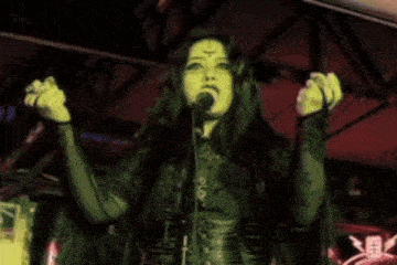 a woman is singing into a microphone while surrounded by skulls .