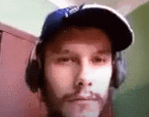 a man wearing headphones and a dodgers hat is looking at the camera