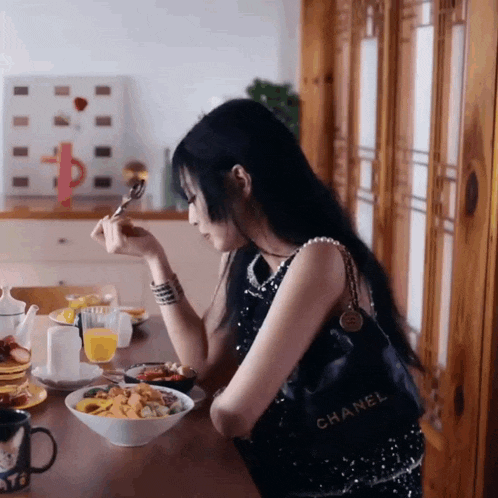 a woman sits at a table with a bowl of food and a chanel bag