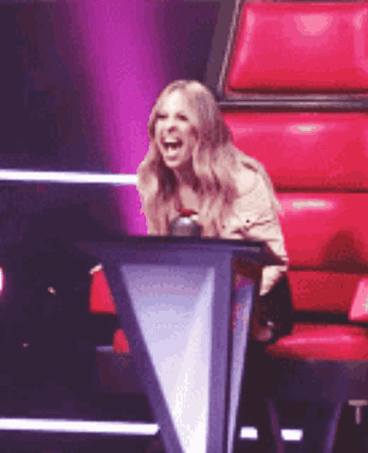 a woman is laughing while sitting in a red chair on a stage