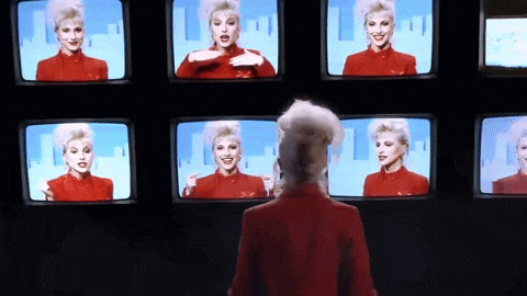 a woman in a red suit stands in front of a wall of televisions