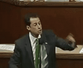 a man in a suit and tie is giving a speech and the word kudos is on the screen