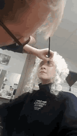 a woman wearing a black sweater that says ' heavy weight ' on it is getting her makeup done