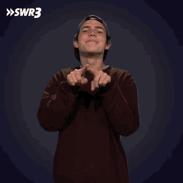 a man wearing a hat and a maroon sweater is pointing at the camera with the swr3 logo behind him